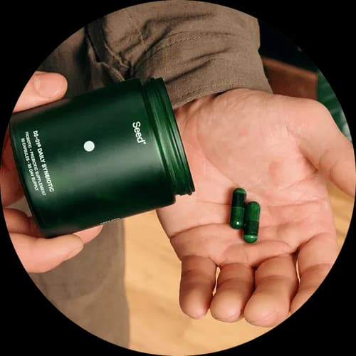 Hand holding a green container with pills