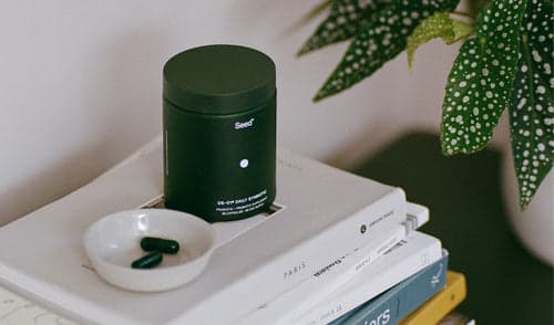 Dark green supplement container with pills on books