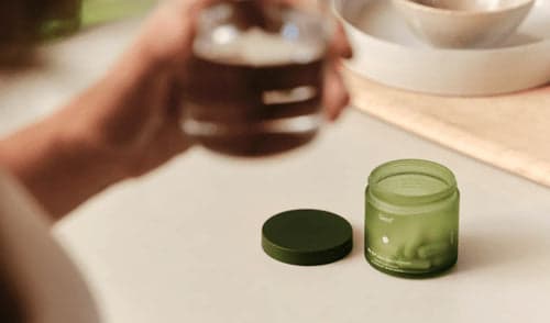 Person holding a glass container with a green lid on a light surface