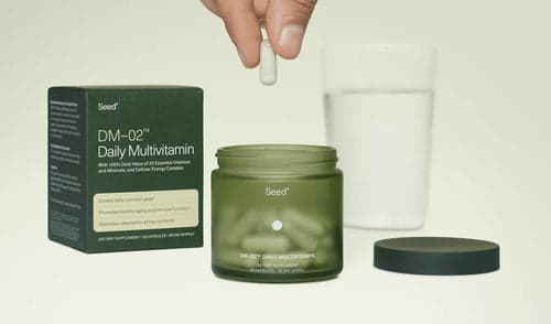 Seed Daily Multivitamin jar with packaging and a hand holding a capsule